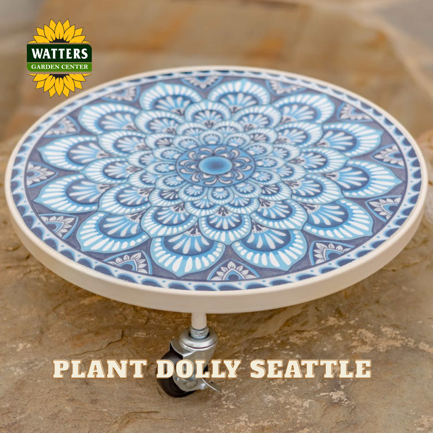 A round ceramic planter plate with a blue and white mandala pattern, mounted on a small wheeled stand, set against a stone background. The Watters Gardens Center logo is visible in the top left, and 'PLANT DOLLY SEATTLE' is written at the bottom.