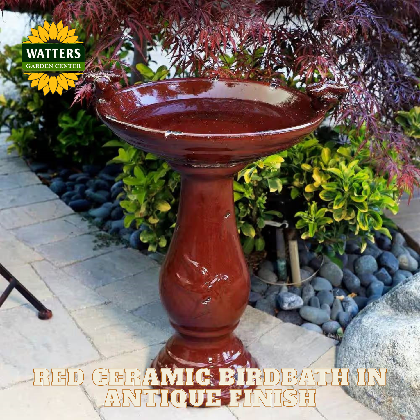 Red ceramic birdbath with antique finish in a garden setting, featuring Watters Garden Center logo.