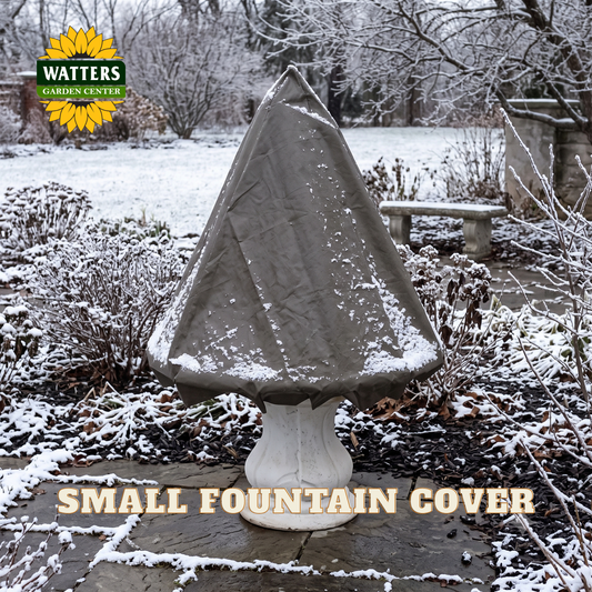 A small garden fountain cover by Watters Gardens Center, shown outdoors in a snowy landscape. The cover is draped over a white pedestal fountain, with snow on the ground and bushes in the background.