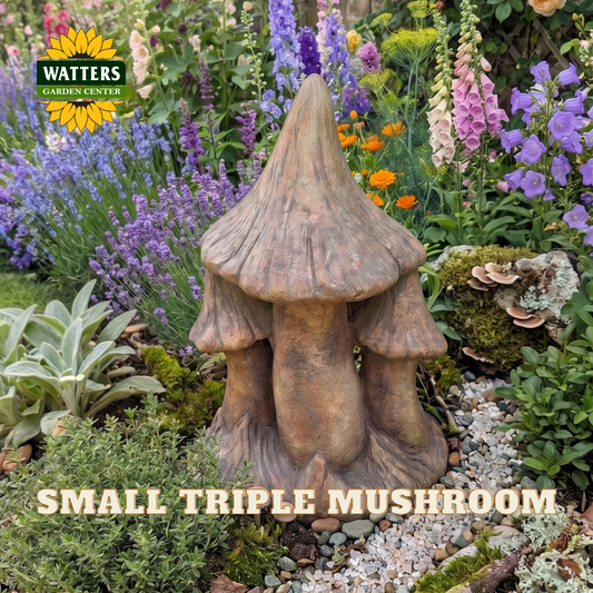 A small triple mushroom garden statue in a natural brown faux-stone finish, displayed in a colorful garden bed with purple flowers, green foliage, and moss. The Watters Gardens Centre logo is visible in the top left, and 'SMALL TRIPLE MUSHROOM' is written in text at the bottom.