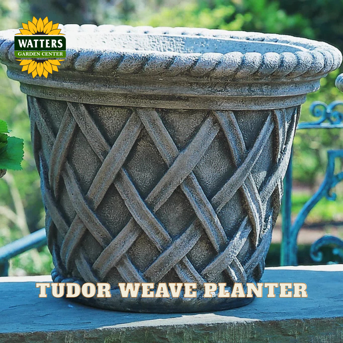 A gray faux-stone planter with a woven basket pattern and a rope-textured rim, shown outdoors on a stone ledge with green garden foliage in the background. A Watters Garden Center logo is in the top-left corner, and 'TUDOR WEAVE PLANTER' is written across the bottom.