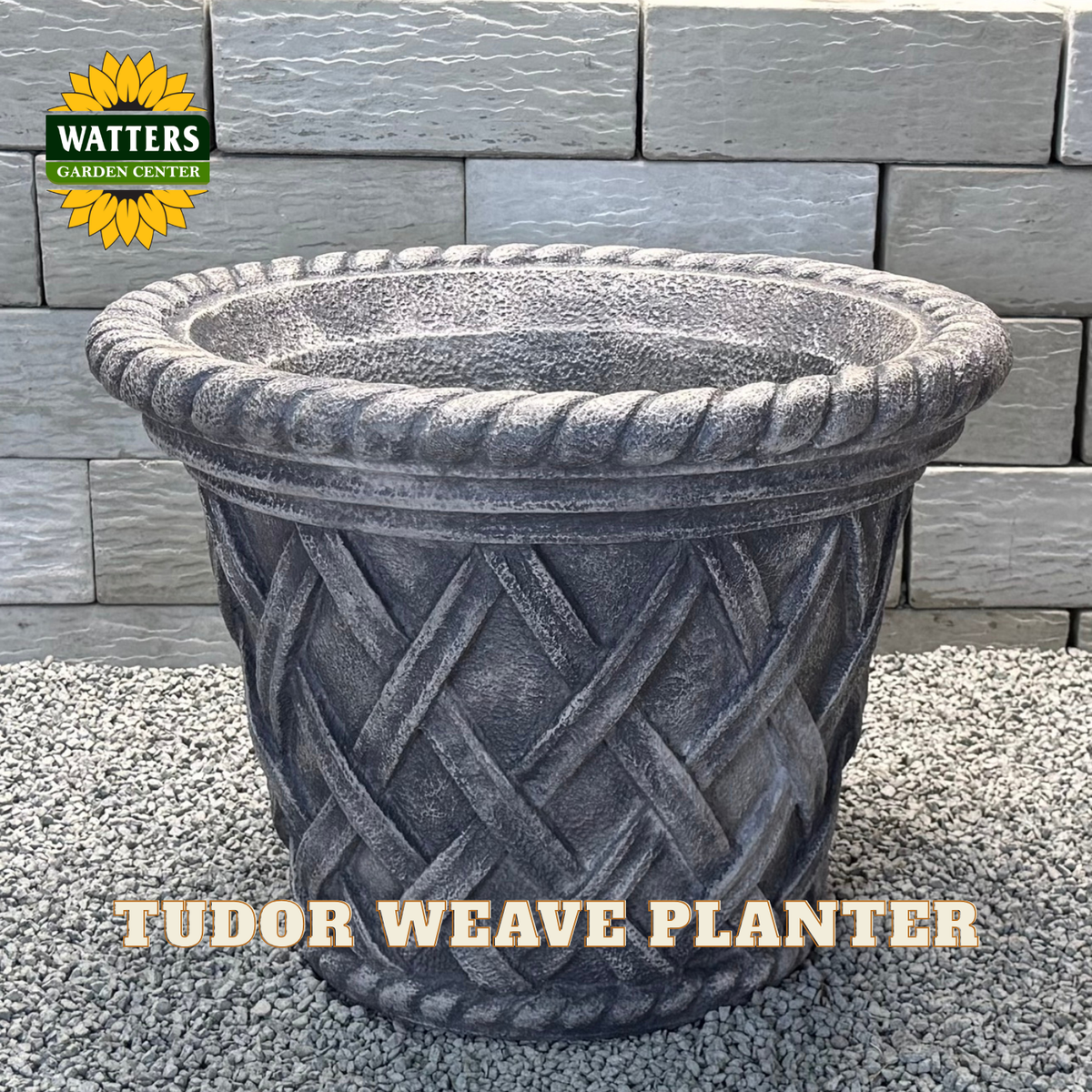 A large gray faux-stone planter with a rope-tied rim and a textured lattice pattern on the body, shown outdoors against a gray brick wall and gravel ground. The Watters Garden Center logo appears in the top-left corner, and the text 'TUDOR WEAVE PLANTER' is overlaid at the bottom.