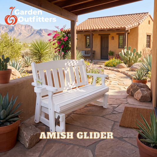 A white wooden Amish glider bench with a side cup holder, set on a stone patio under a covered porch with a desert house and mountains in the background. The text 'AMISH GLIDER' is displayed at the bottom, and the '7 Garden Outfitters' logo is in the top left corner.