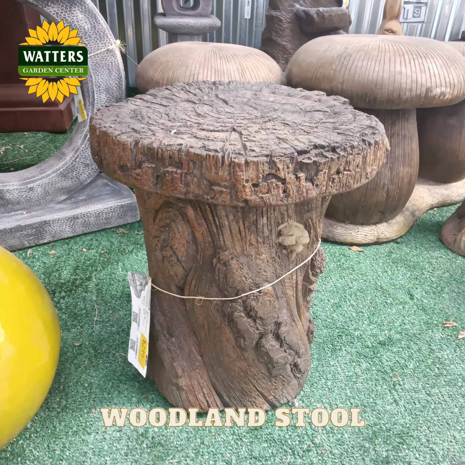 Wooden stool with a tag labeled 'Watters Garden Center' on a green surface.