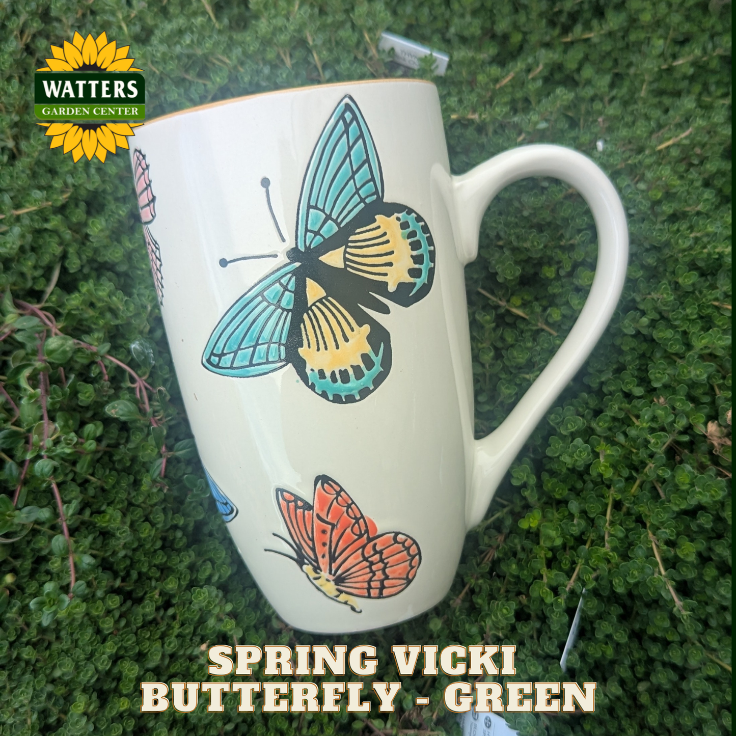 White mug with butterfly design on a green grass background, featuring Watters Garden Center branding.